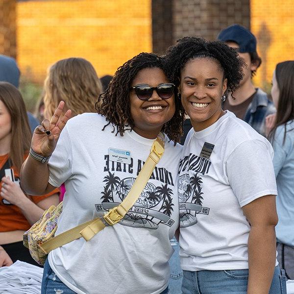 Two students wearing black and white Spring Week t-shirts smile for the camera.