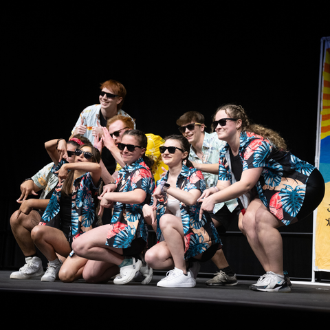 A group of students dressed in matching Hawaiian shirts and sunglasses perform a choreographed dance on stage during the Sycamore Sync Sessions event at Indiana State University.